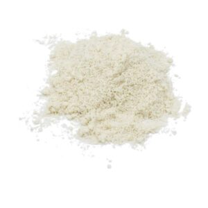 A pile of finely ground Almond Flour is spread on a white background. The flour is off-white to light beige in color, with a slightly irregular texture and smaller grains scattered around the main heap, giving it a natural, unprocessed appearance.